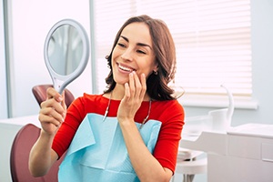 Woman in red shirt smiling at reflection in dentist's mirror