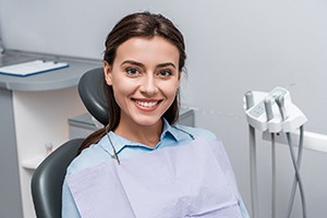 Smiling woman sitting in dental chair with new dental bridge in Springfield, IL