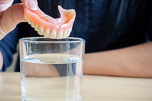 hand putting denture into a glass of water