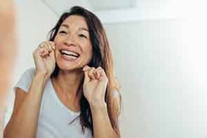 a woman flossing her teeth for dental implant care